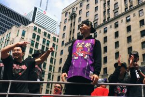 smiling Jeremy Lin in Raptor uniform atop of vehicle by men during daytime