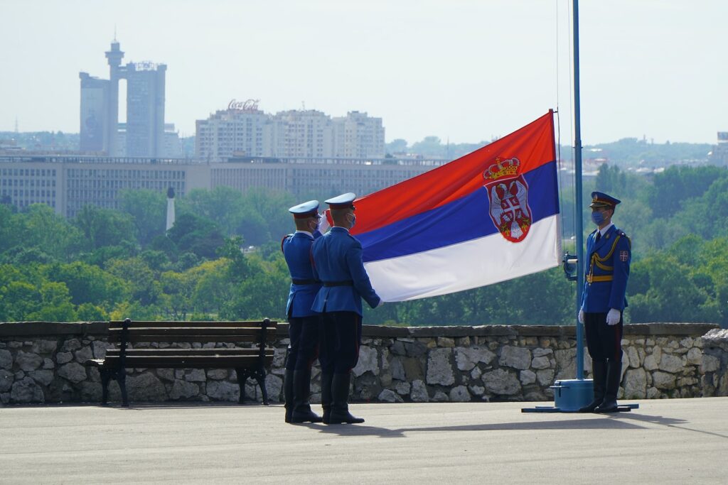 man in black jacket standing near flag of us a during daytime Serbia 塞爾維亞 賽爾維亞 塞國 武契奇 科索沃北部車牌事件