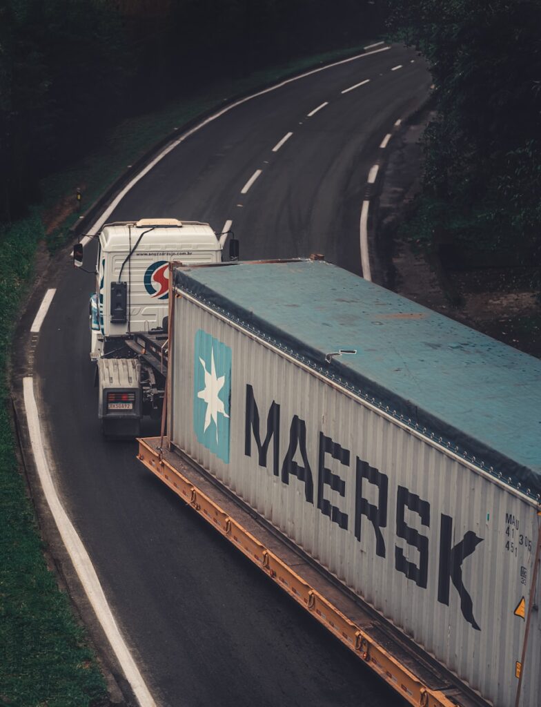 馬士基（Maersk） a semi truck driving down a road next to a forest