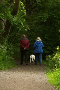 man and woman with white dog walking on dirt road during daytime